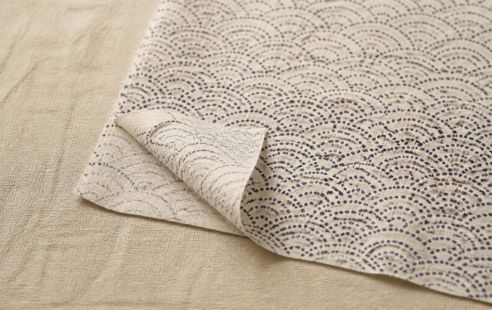 Traditional Japanese tenugui, a flat plain-weave cotton hand cloth with indigo seigaiha wave pattern, one corner folded to show the thin single-layer weave